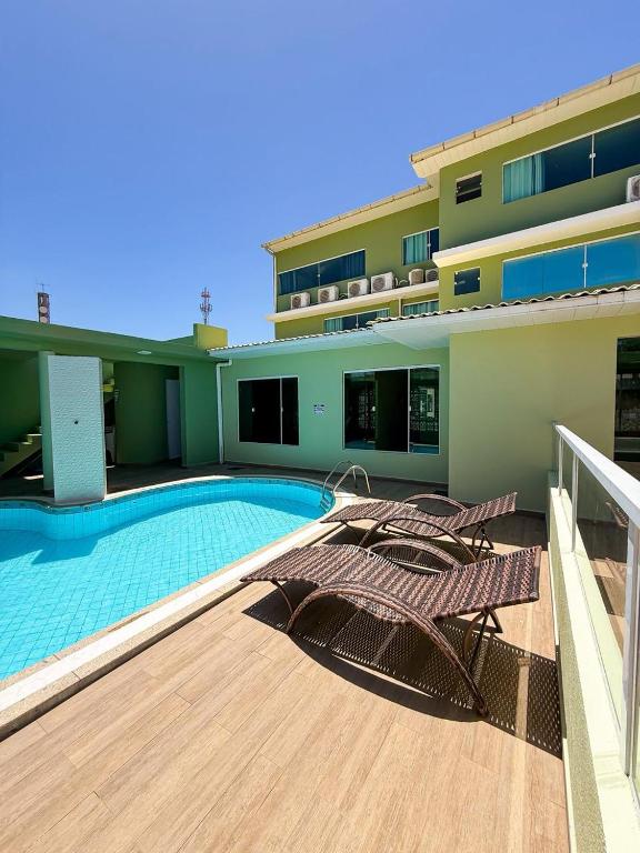 a building with a swimming pool and two chairs on a deck at Amaliê Pousada in Barra de São Miguel