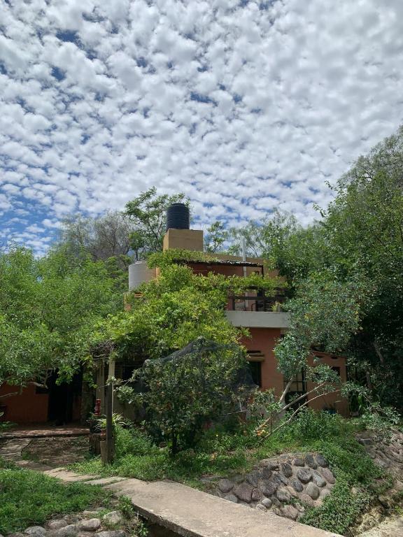 a house under a cloudy sky with trees in front at Espacio Kaskai in San Marcos Sierras