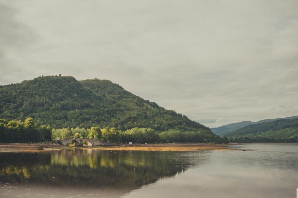 a mountain with a reflection in the water at NICHT' Apartments Inveraray Town Centre in Inveraray