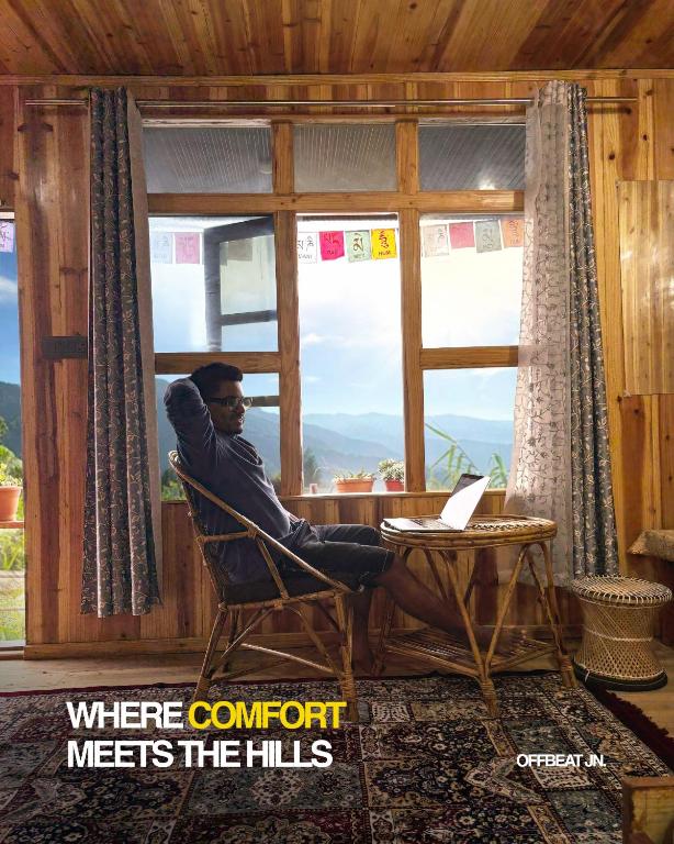 a man sitting in a chair looking out of a window at Offbeat Jn in Sukhia Pokhari