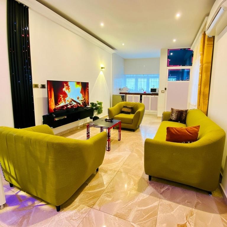 a living room with yellow chairs and a tv at Eliass Palace in Cotonou