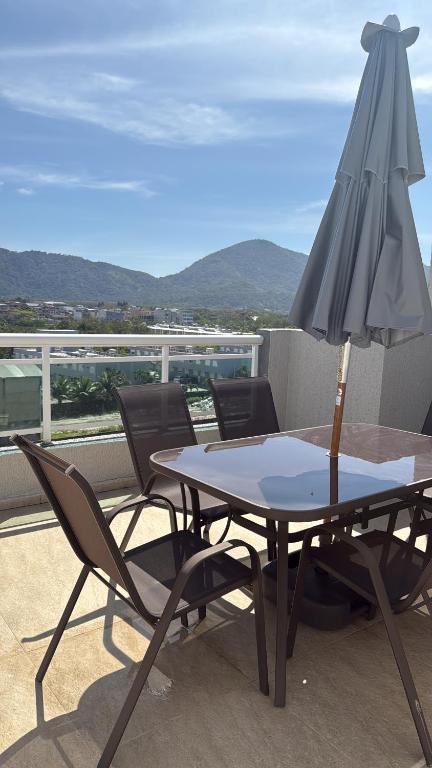 una mesa con sillas y una sombrilla en el balcón en Cobertura Linear no Recreio - Varanda Grande, Vista Montanhas, Próx Praia, Garagem, Acomoda até 4 pessoas, en Río de Janeiro