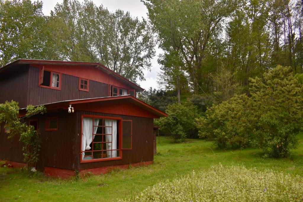 een klein rood huis in een veld met bomen bij Casa Maqui Salto del Laja in Salto del Laja
