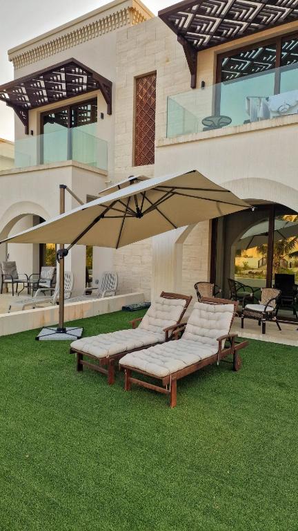 a group of lounge chairs under an umbrella on a lawn at Hawana Salalah Poolside Apartment in Salalah