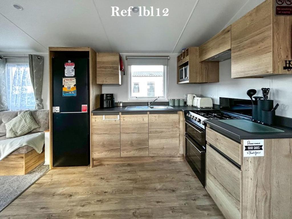 Una cocina con gabinetes de madera y un refrigerador negro. en Parkdean Resort Camber Sands sleeps 8 Pet Friendly - ref-lbl12, en Camber