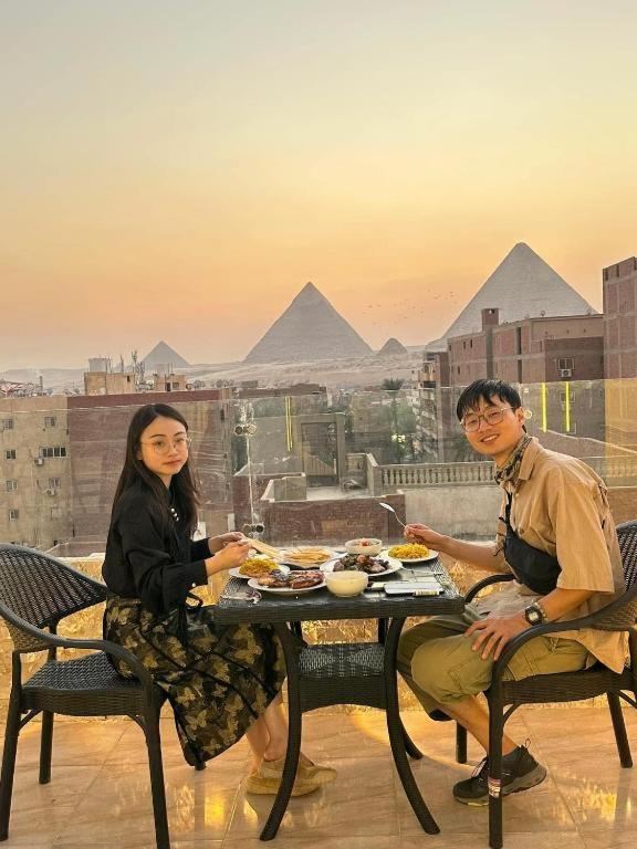 开罗boulevard Pyramids view inn的坐在金字塔前桌边的男人和女人