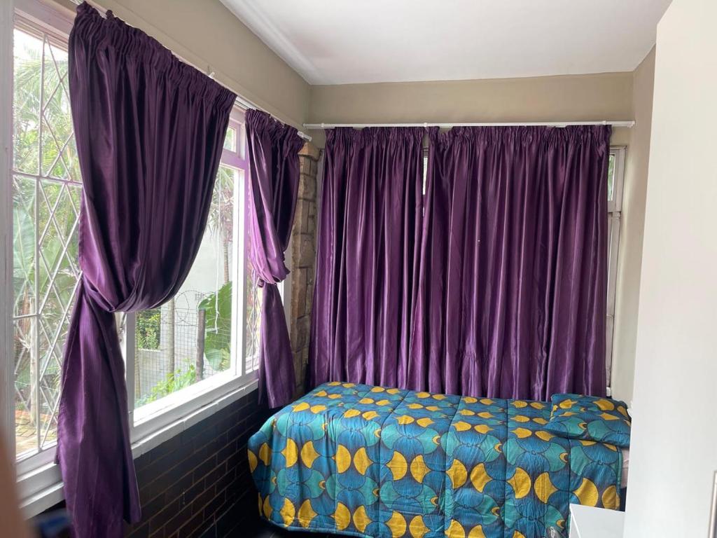 een slaapkamer met paarse gordijnen en een bed naast een raam bij Back Packer Style in Durban