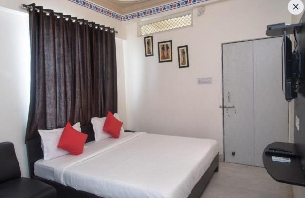 a bedroom with a bed with red pillows and a television at HOTEL ARAWALI UDAIPUR CITY BEST couples friendly stay in Udaipur
