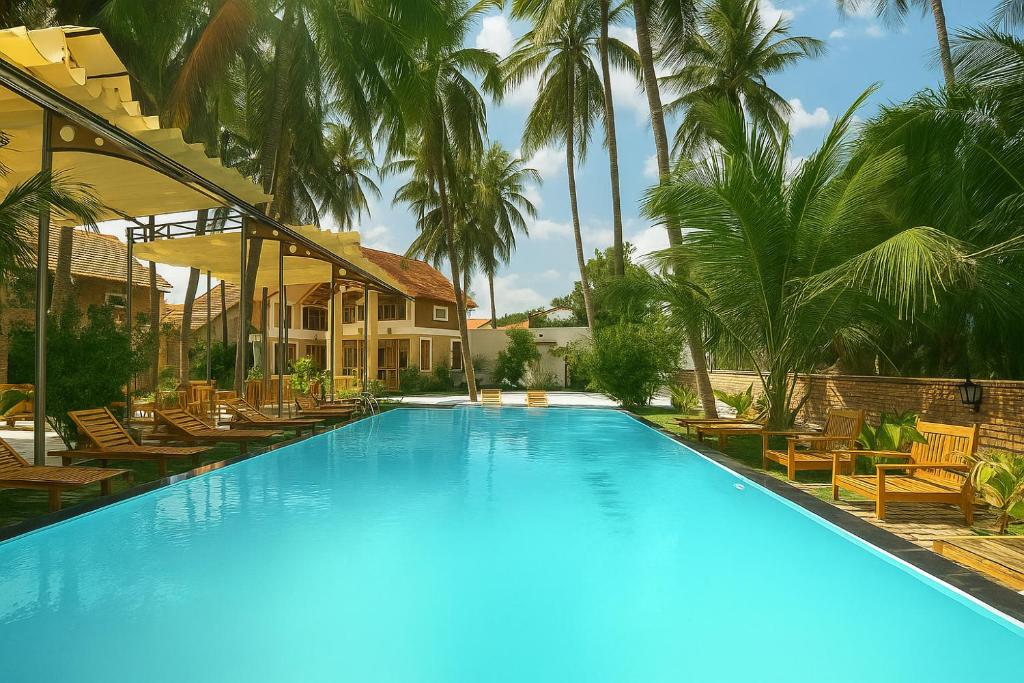 a large swimming pool with chairs and palm trees at Coconut Garden Mui Ne in Mui Ne