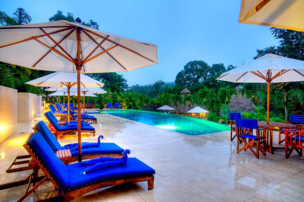 a group of chairs and umbrellas next to a swimming pool at The Lodge at ChaaCreek in San Ignacio