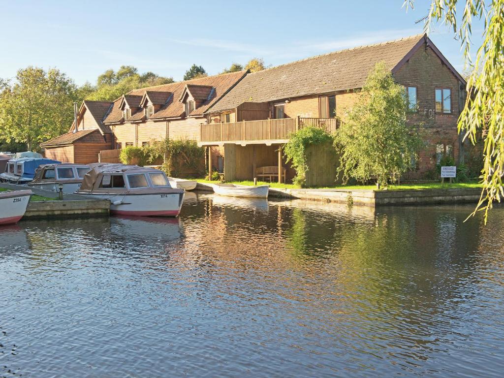 une maison avec des bateaux amarrés dans l'eau en face dans l'établissement Coot Cottage, à Dilham