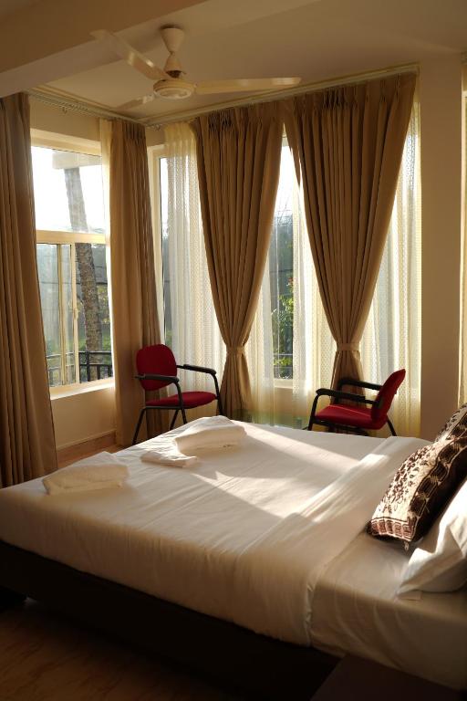a bedroom with a large bed with two chairs and windows at The Thekkady Haritham Residency in Thekkady