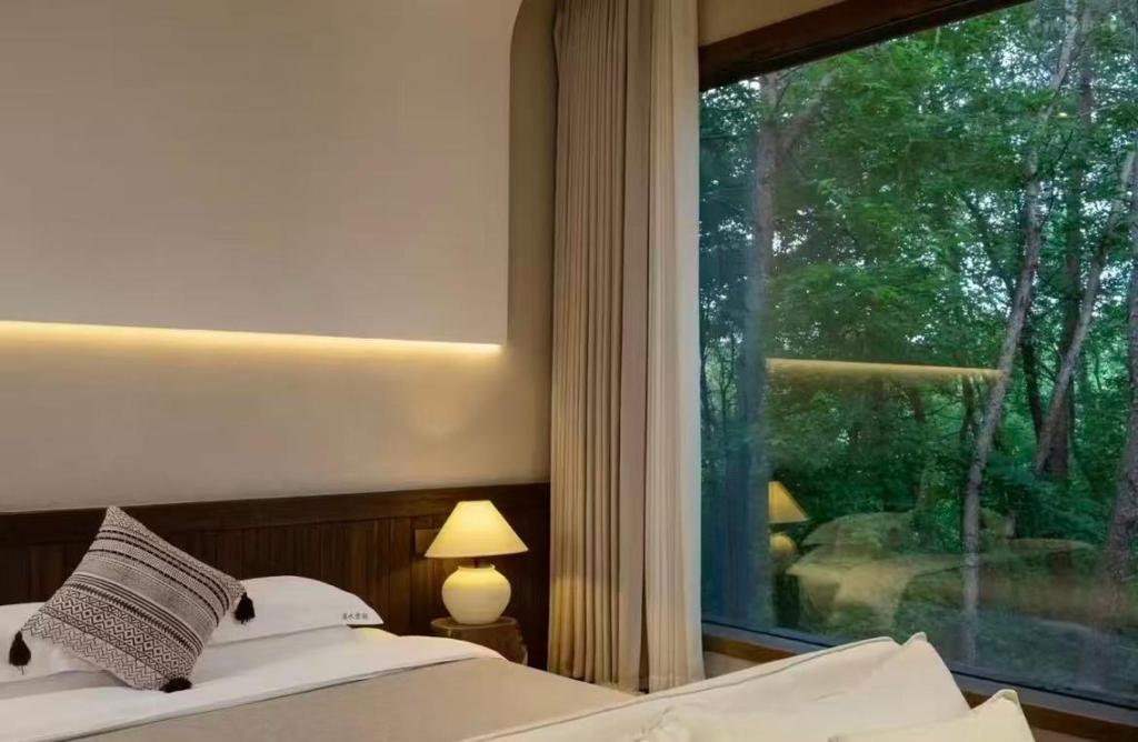 a bedroom with a bed and a large window at Huangshan Xishui Yunjian Forest Resort Hotel in Huangshan