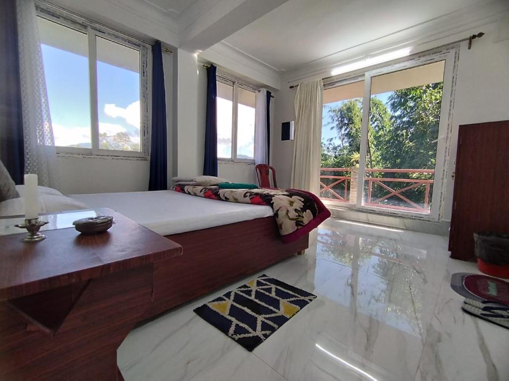 a bedroom with a bed and a table and windows at Marmen Homestay in Kalimpong