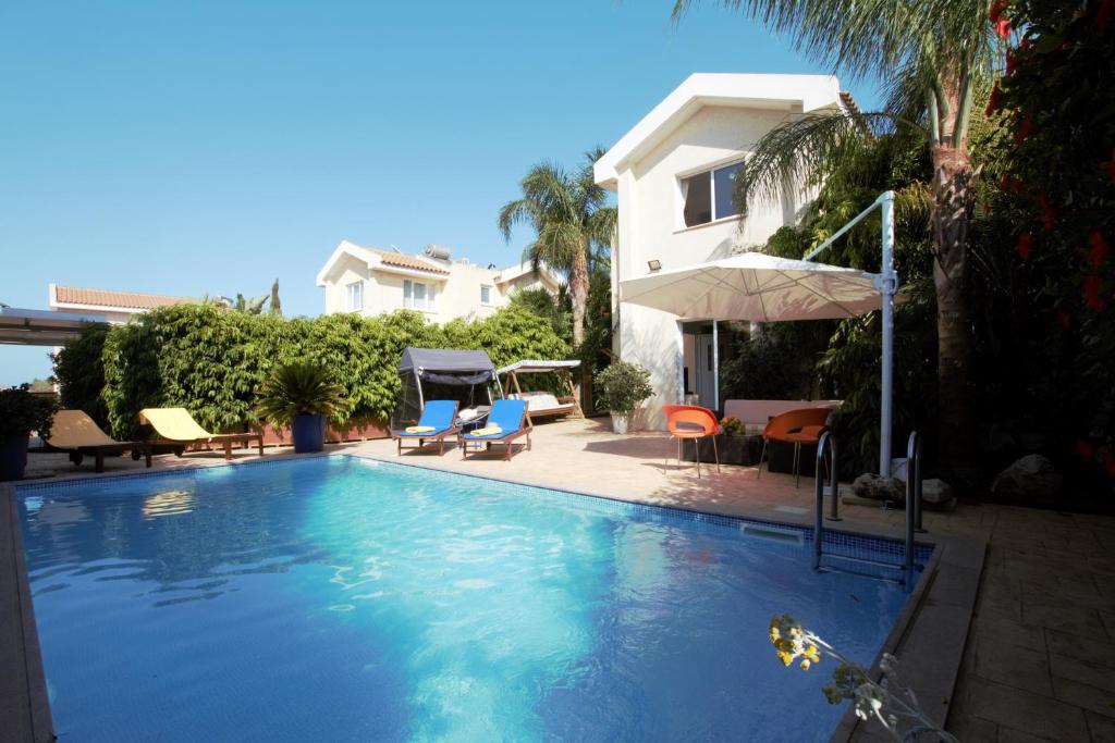a swimming pool with chairs and an umbrella next to a house at Helene Villa in Protaras