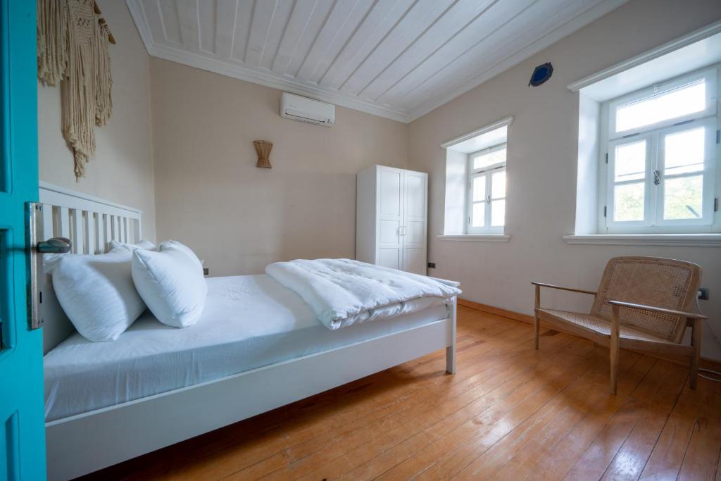 a bedroom with a bed and a chair and two windows at MINIQ HOMES 103 - Stone House with Garden Cinema, Barbecue, Mini Golf in Foca