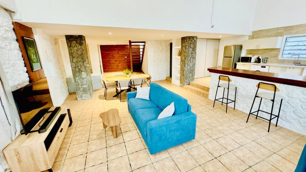 Una sala de estar con un sofá azul y una cocina. en Chez Nat&Jo, en Le Bois de Nèfles