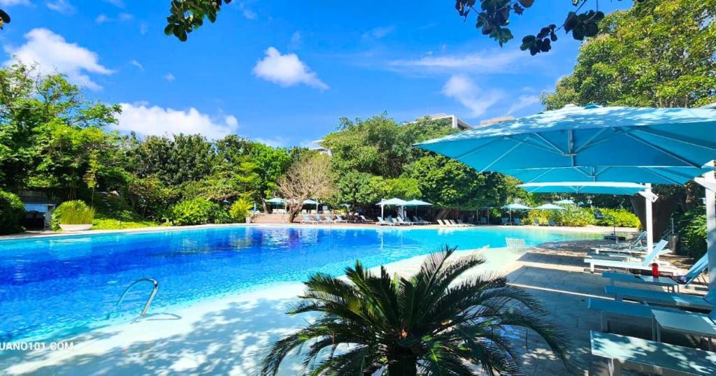 a large swimming pool with an umbrella and chairs at TDJ Japandi Room with Residential Pool access in Tambuli Seaside Mactan in Maribago