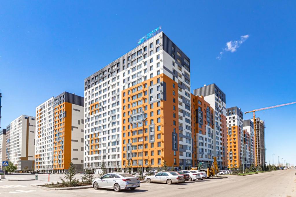 a tall building with cars parked in a parking lot at Apartment near Astana Arena in Taldykolʼ