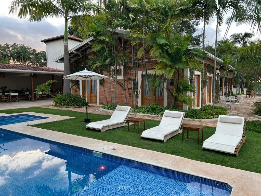 eine Villa mit einem Pool, Stühlen und einem Haus in der Unterkunft Pousada Manacá Exclusive Suítes in Rifaina