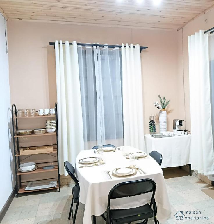 a dining room with a table with chairs and white curtains at Maison Andrianina in Ampitatafika