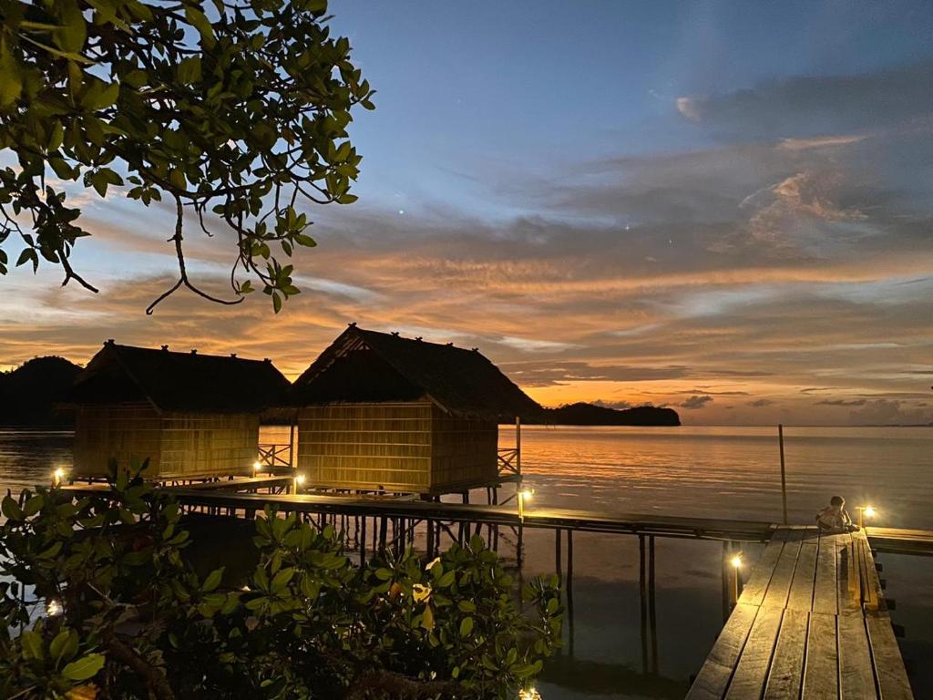 a house on a dock with a sunset over the water at Batanta Guest House in Pulau Birie