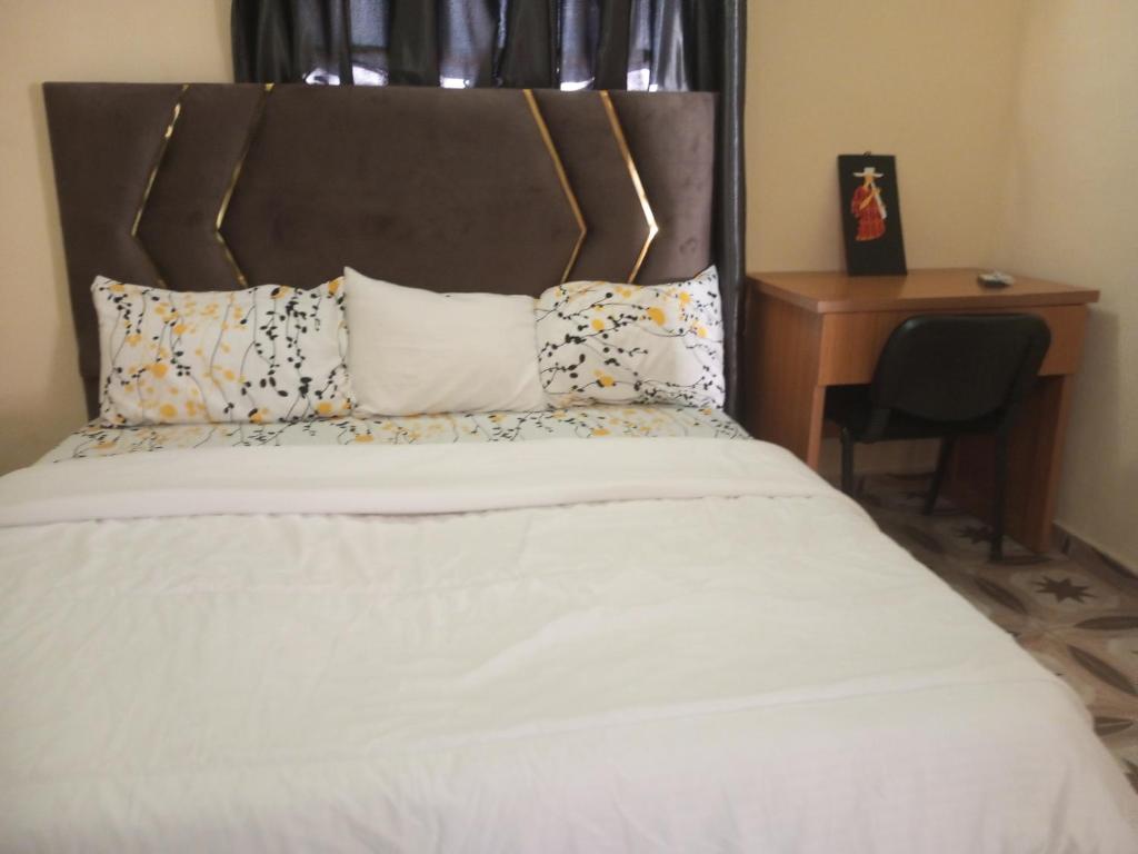 1 cama con sábanas blancas y almohadas junto a un escritorio en Richbee Hotel and Suites, en Abuja