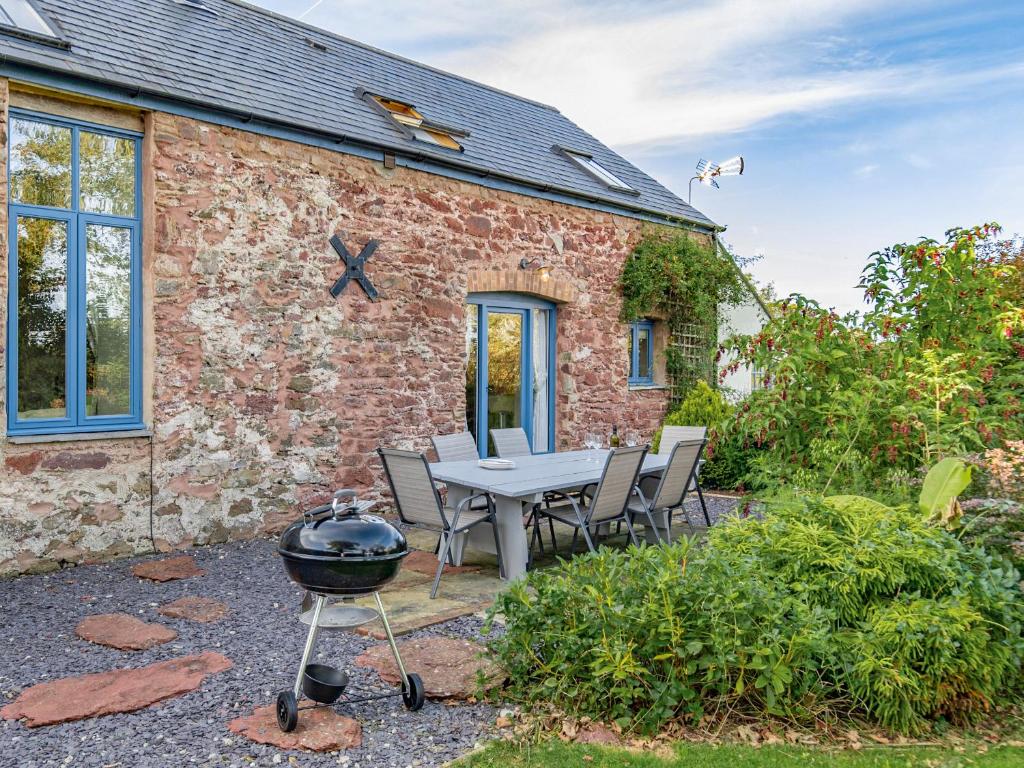 a brick house with a table and chairs and a grill at The Old Cowshed in Saint Ishmaels