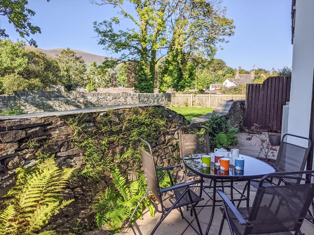 a table and chairs on a patio with a stone wall at 2 Greta Grove House in Keswick