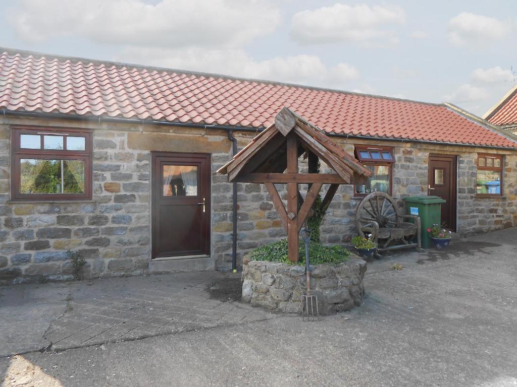 a stone house with a wooden structure in front of it at Swallows Nest-18094 in Cloughton