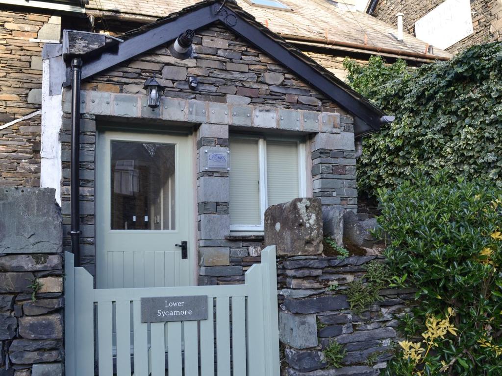 ein Cottage aus Stein mit einem weißen Zaun und einer Tür in der Unterkunft Lower Sycamore Cottage in Ambleside