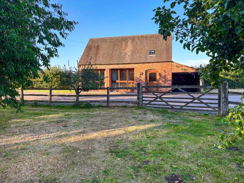 un antiguo granero de ladrillo con una valla delante en The Old Carthouse, en Abbots Bromley