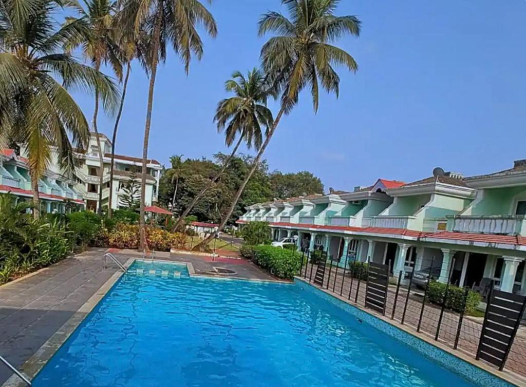 a pool in front of some buildings with palm trees at Modern 2BHK Hideout in Benaulim in Benaulim