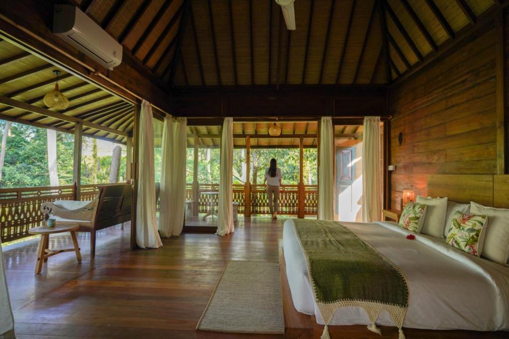 a bedroom with a bed and a woman standing on a balcony at The Shala Bali in Ubud