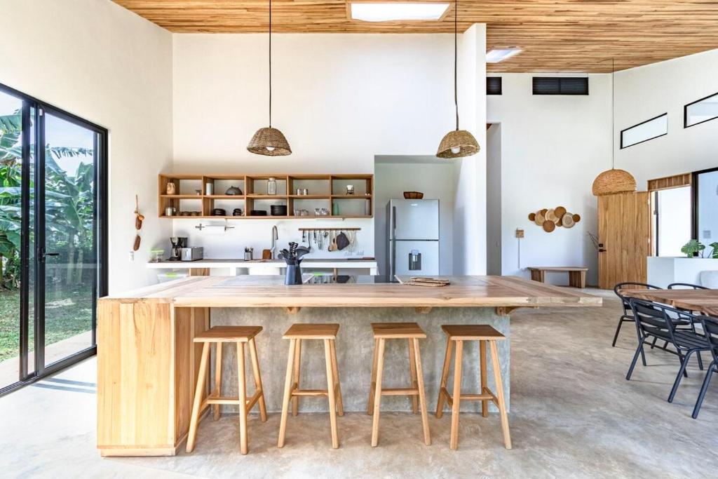 an open kitchen with a large wooden table and stools at Private rainforest villa up to 8 guests w jacuzzi near Rio Celeste in Upala