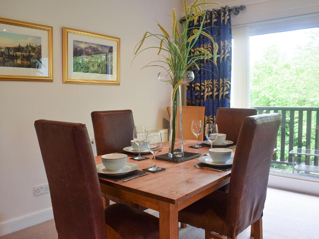 einem Holztisch mit Stühlen und einem Tisch mit einer Vase darauf in der Unterkunft Treetops in Bowness-on-Windermere