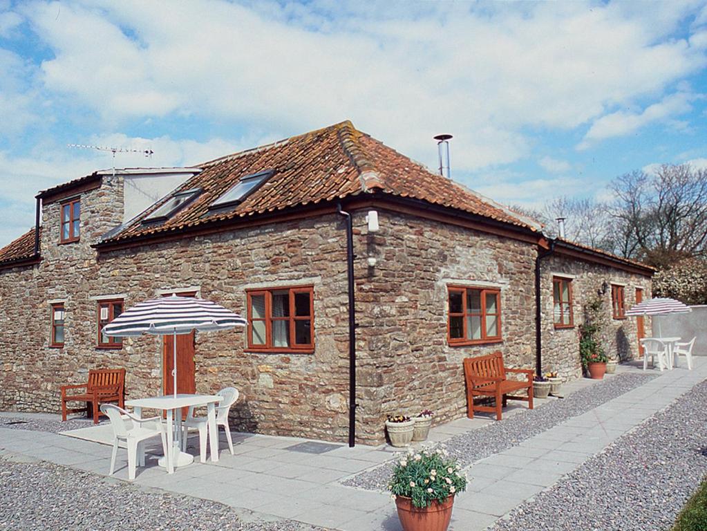 a stone house with a table and chairs and an umbrella at Barrowmead Cottage - E2377 in Banwell