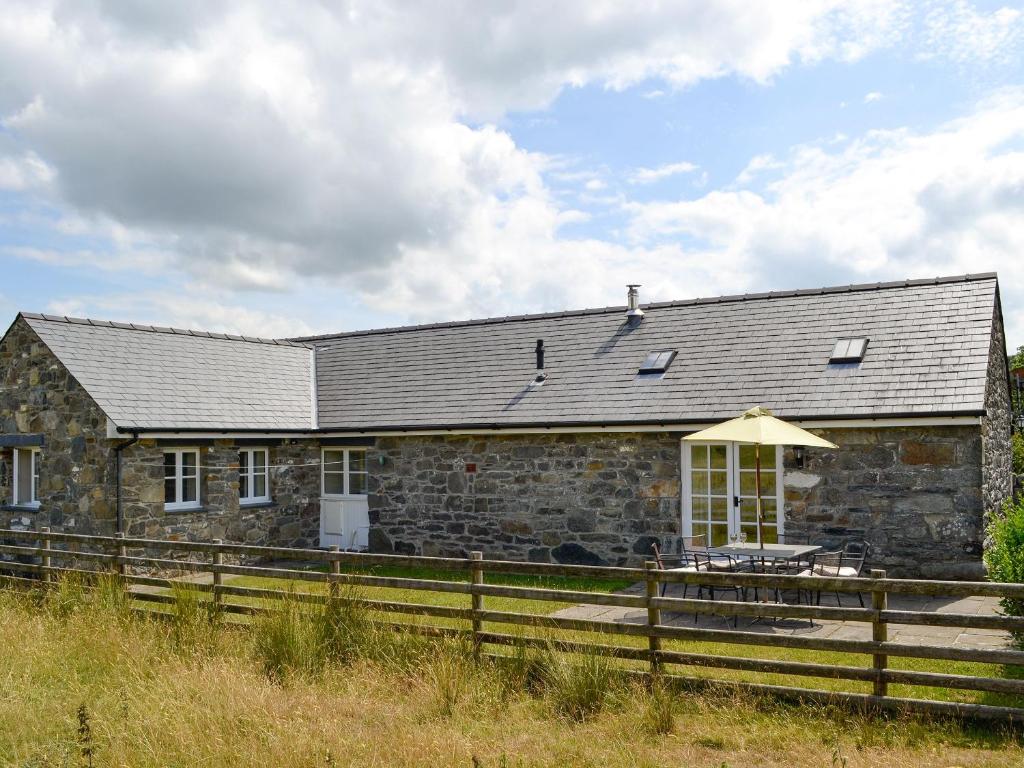 a stone house with a table and an umbrella at Sgubor Ucha in Trefriw