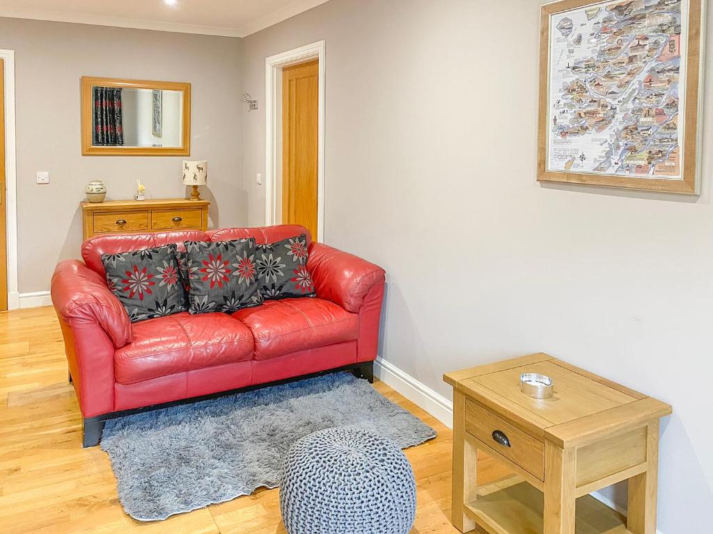 ein rotes Ledersofa im Wohnzimmer mit einem Tisch in der Unterkunft Dalnafeidh Beag - Cottage in Portnacroish