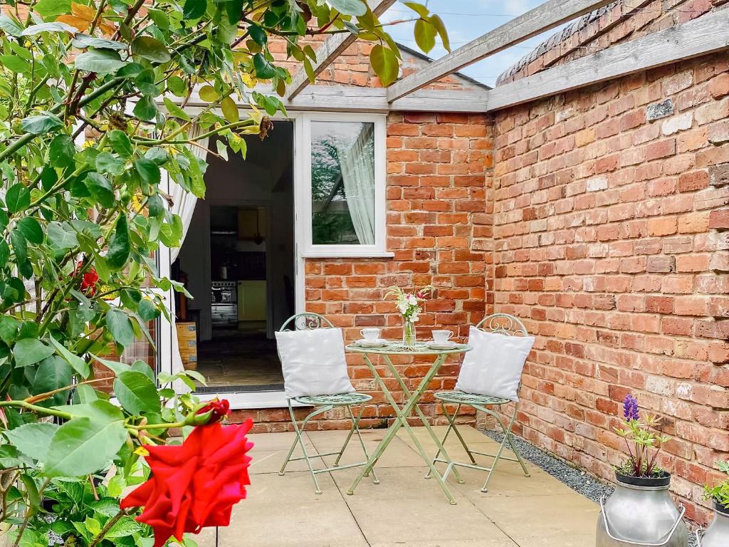 a patio with a table and two chairs and a brick wall at The Parlour in Earls Croome