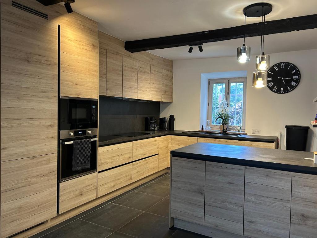 a kitchen with wooden cabinets and a clock on the wall at Maison de la Fontaine in Hierges