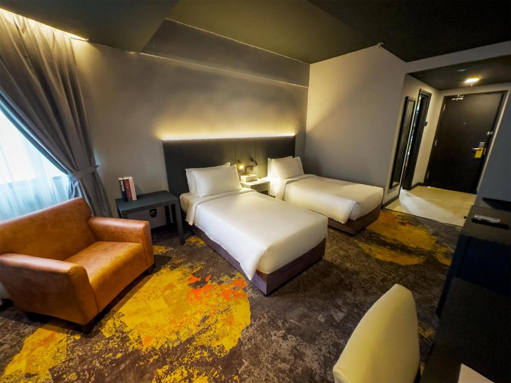 a hotel room with two beds and a chair at Trigo Hotel Kuala Lumpur in Kuala Lumpur