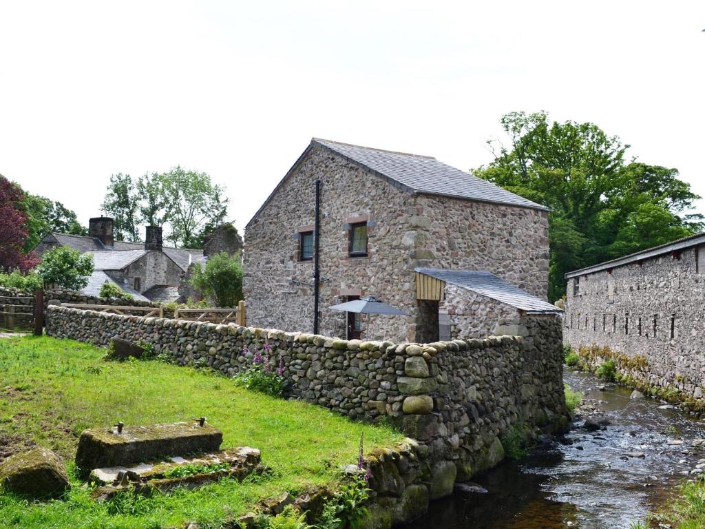 ein Steinhaus mit einer Steinmauer neben einem Fluss in der Unterkunft Shepherds Cottage in Corney