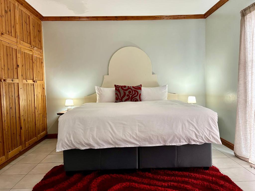 a bedroom with a large white bed with a red rug at Colline Sainté Cottage in Port Alfred