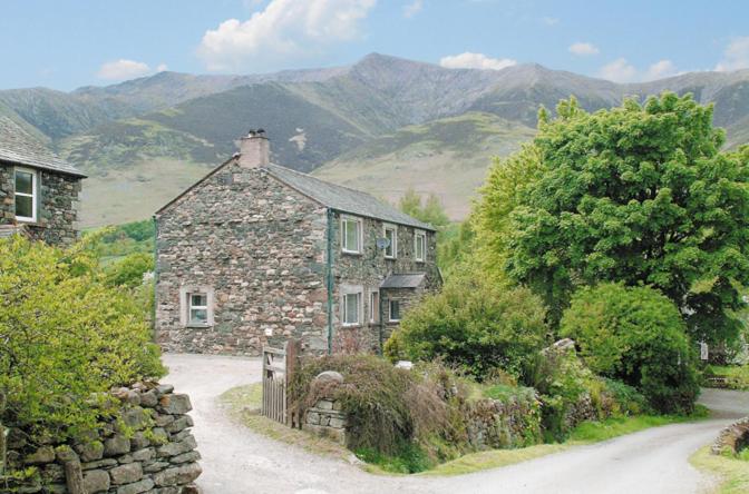 an old stone house on a road with mountains in the background at Netherend in Threlkeld