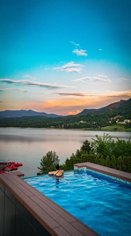 a person laying in a swimming pool overlooking a lake at Hotel Roser House Boutique - pe malul lacului Colibita in Colibiţa
