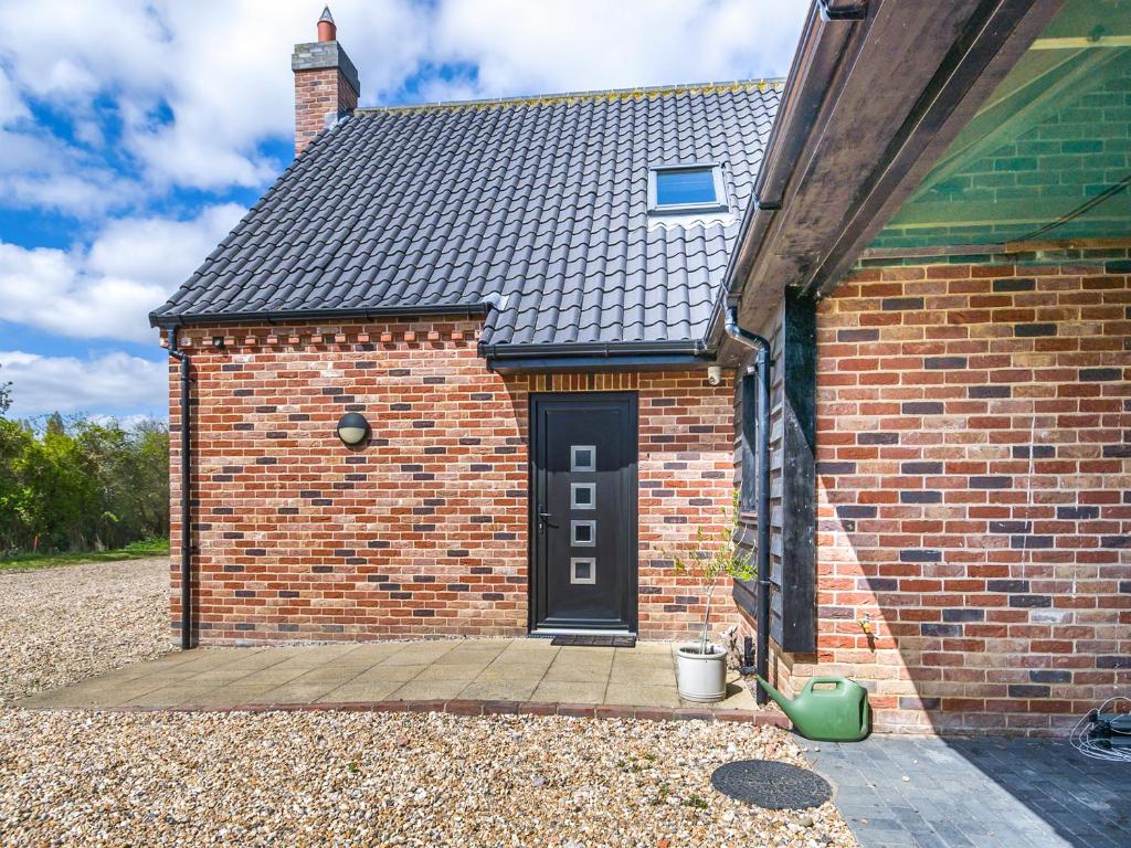a brick house with a black door and a wooden porch at The Paddocks in Lowestoft