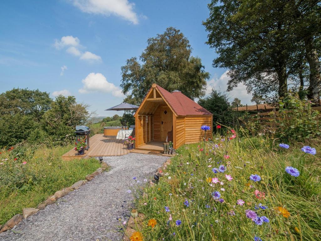 a small wooden cabin with a wooden deck and flowers at Dol Y Mynydd The Mountain Meadow - Cottage in Llangernyw