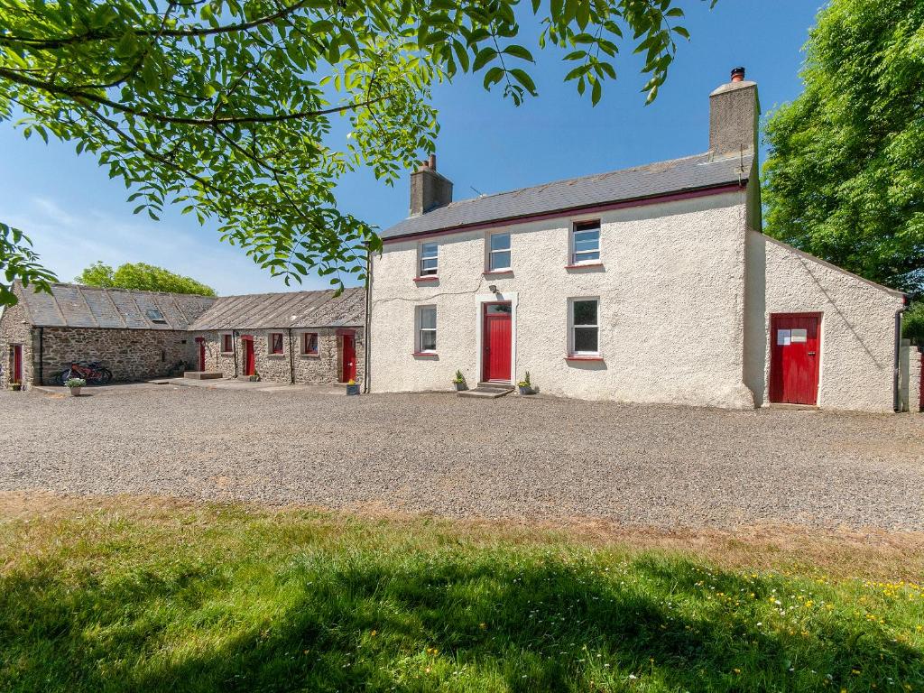 un vieux bâtiment blanc avec des portes rouges sur une allée de gravier dans l'établissement Ffynnonddewi Farmhouse - Qc1535, à Llanhowell