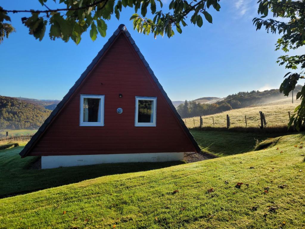 a red house on a hill with a green field at Highland Glen Lodges in Rogart